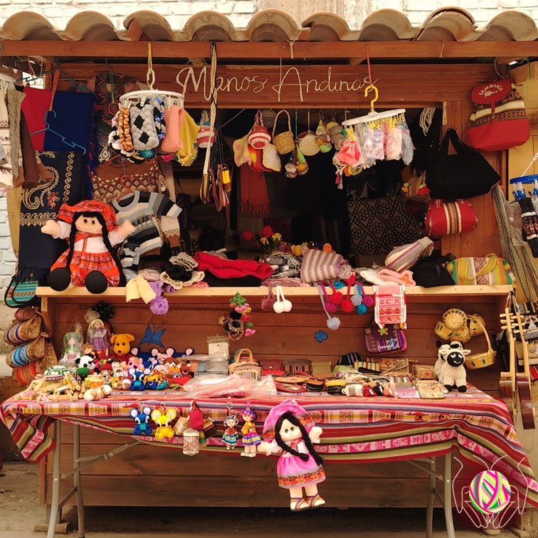 Vista frontal de la caseta de la tienda "Manos Andinas", exhibiendo coloridas artesanías peruanas y productos hechos a mano, ubicada en Bambamarca, Cajamarca, Perú.