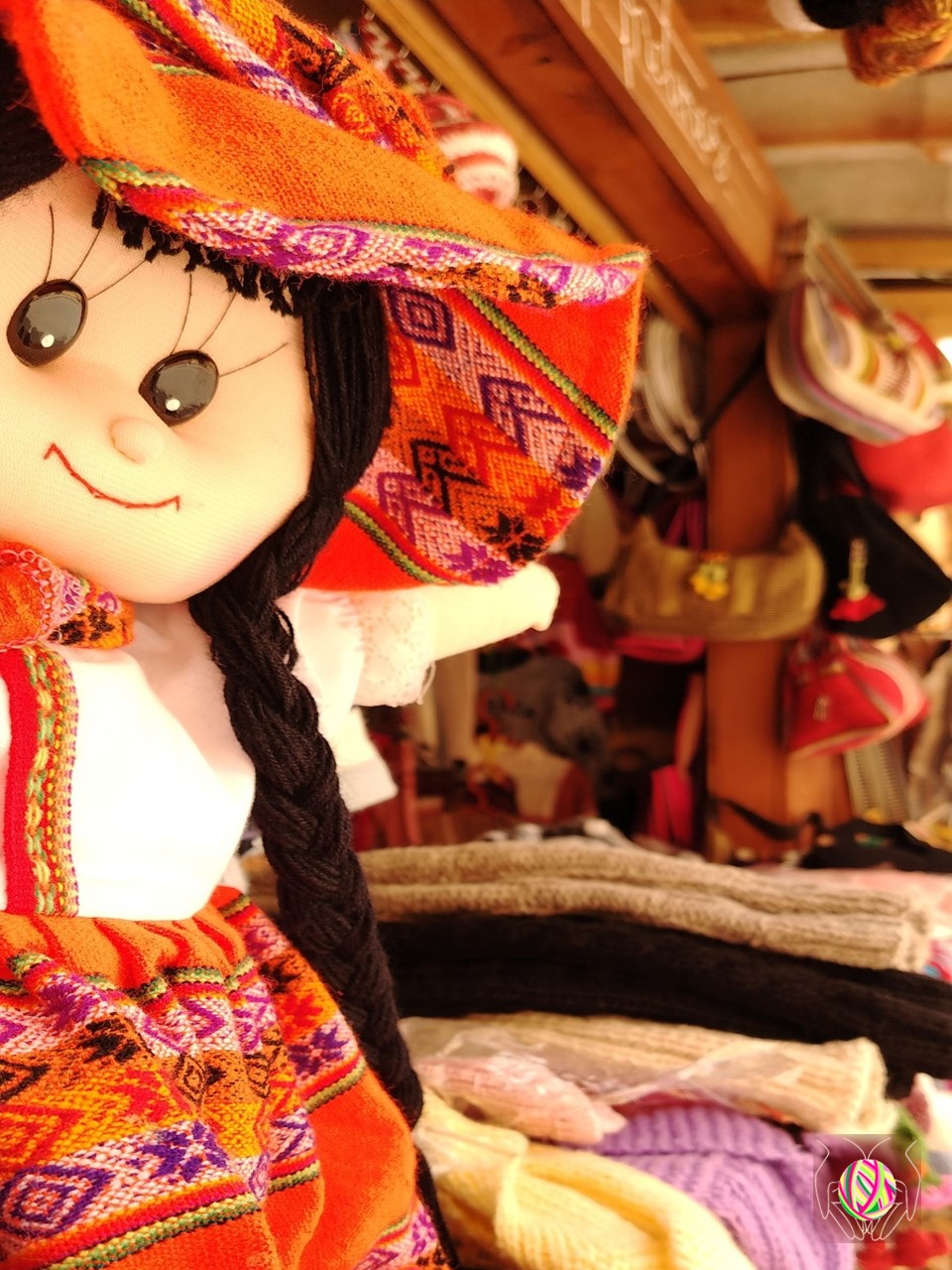 Muñeca artesanal de "Manos Andinas" en primer plano, con otras artesanías peruanas tradicionales en el fondo, representando la riqueza cultural de Cajamarca, Perú.